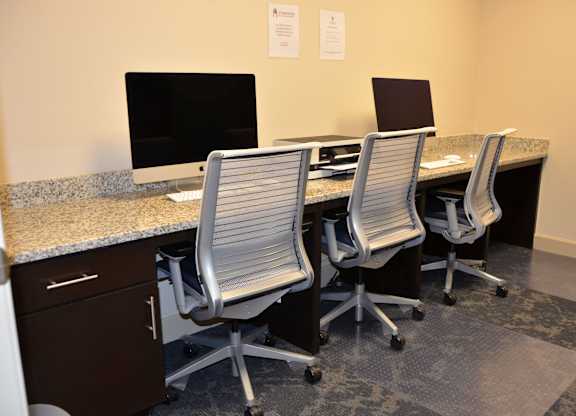 Three chairs are arranged around a desk with two computer monitors and a printer.
