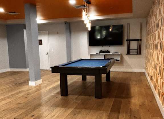 A pool table in a room with wooden flooring and a television mounted on the wall.