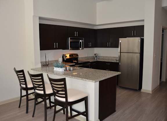 A kitchen with a white counter top and brown chairs.