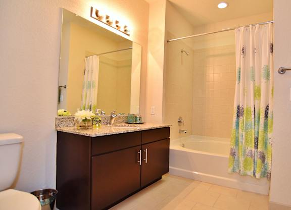 A bathroom with a white tub/shower, toilet, cabinet and mirror.