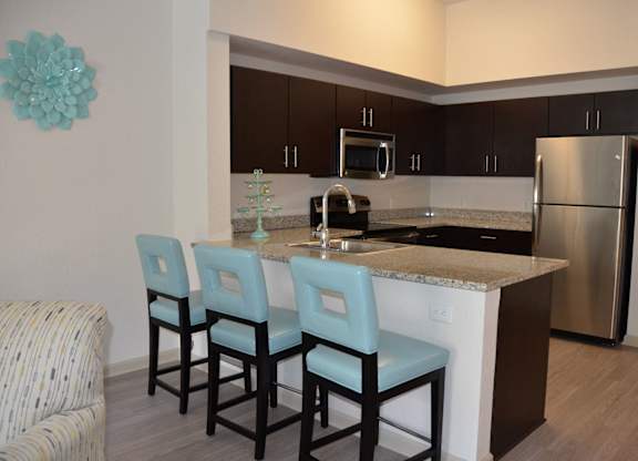 A kitchen with an island, three chairs, and a refrigerator.