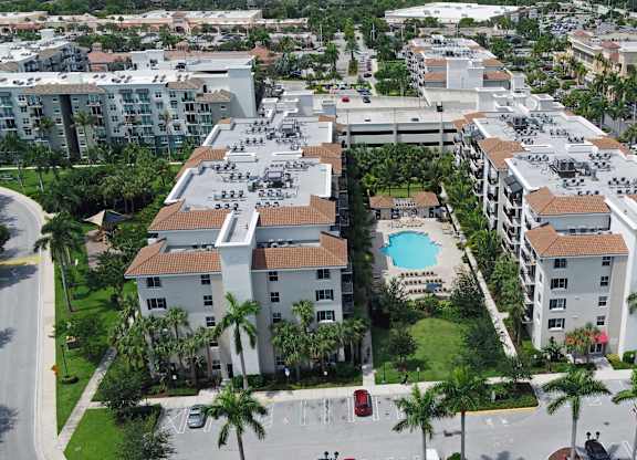A large apartment complex with a pool in the middle of a courtyard surrounded by palm trees.