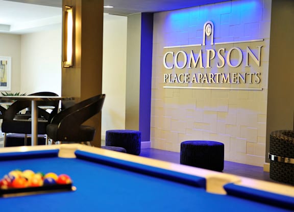 A pool table is in the middle of a room with a sign that says Compson Place Apartments.