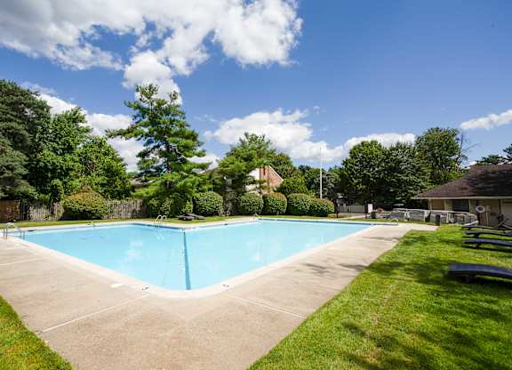A blue swimming pool surrounded by green grass and trees at Brookshire Trace Townhomes Apartments, Pennsylvania