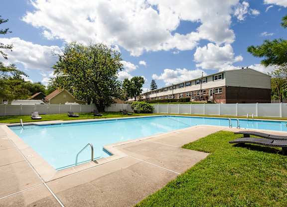 A swimming pool surrounded by a concrete deck and a grassy area with a bench at Brookshire Trace Townhomes Apartments, Pennsylvania
