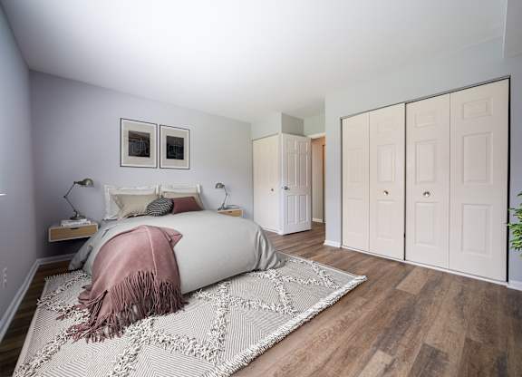 A bedroom with a bed, a pink blanket, a rug, and a plant.