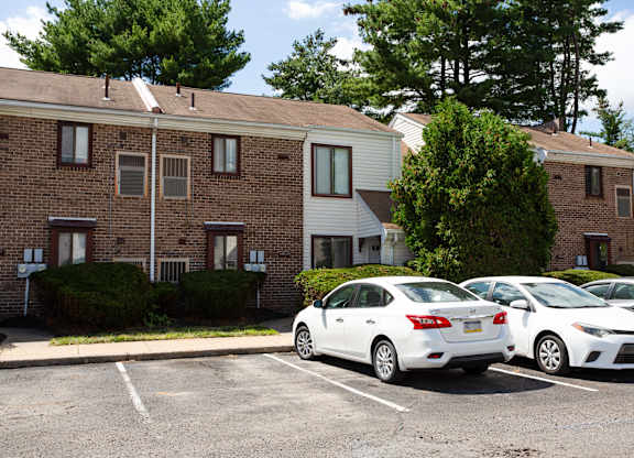 Two white cars parked in a parking lot in front of a brick building at Brookshire Trace Townhomes Apartments, Pennsylvania