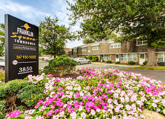 A sign for Franklin Square Townhomes is in front of a building with a flower bed in the foreground.