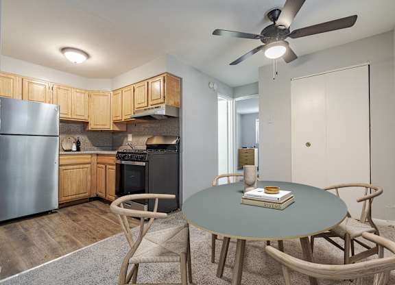 A kitchen with a refrigerator, oven, and a dining table with chairs.