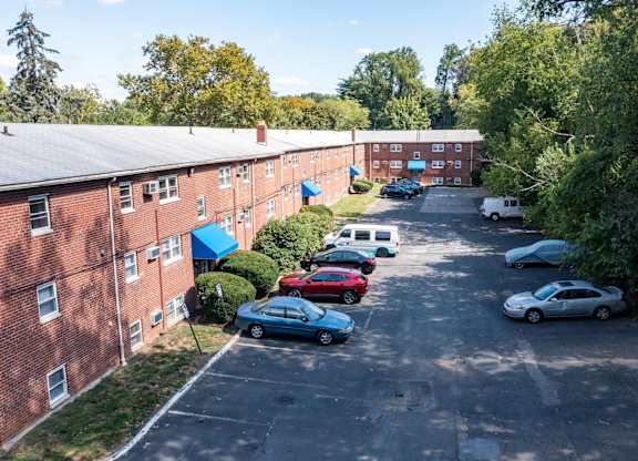 A parking lot with cars parked in front of a red brick building.at Grant Meadows Apartments, Pennsylvania