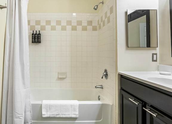 A bathroom with a white tub, black cabinetry, and a shower with a white curtain.at Riverview Landing @ Valley Forge, Eagleville, PA