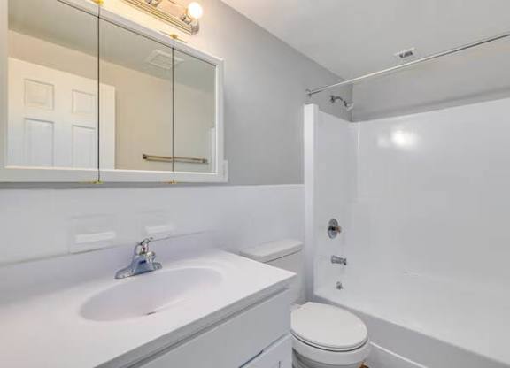 A white bathroom with a toilet, sink, and mirror at Brookshire Trace Townhomes Apartments, Pennsylvania