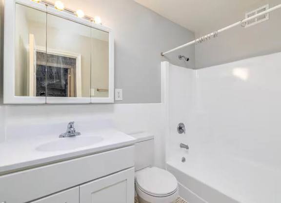 A white bathroom with a toilet, sink, and mirror at Brookshire Trace Townhomes Apartments, Philadelphia, PA