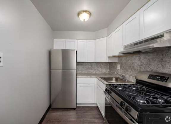 A kitchen with a stainless steel refrigerator, black stove, and white cabinets.at Grant Meadows Apartments, Pennsylvania, 19114