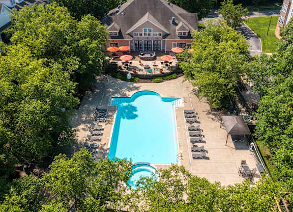An aerial view of a swimming pool surrounded by trees and a building with a patio.