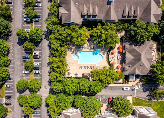 An aerial view of a parking lot with a swimming pool and trees.