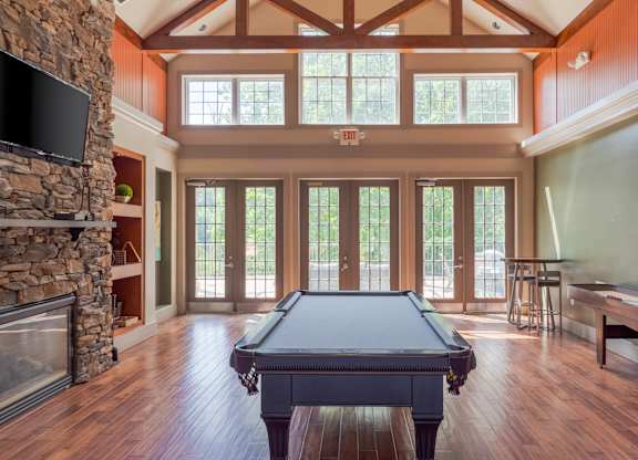 A pool table is in the middle of a room with a stone fireplace and a tv above it.