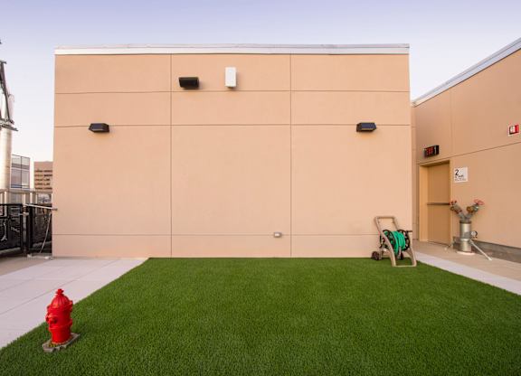 A red fire hydrant is placed on a green lawn in front of a tan building.
