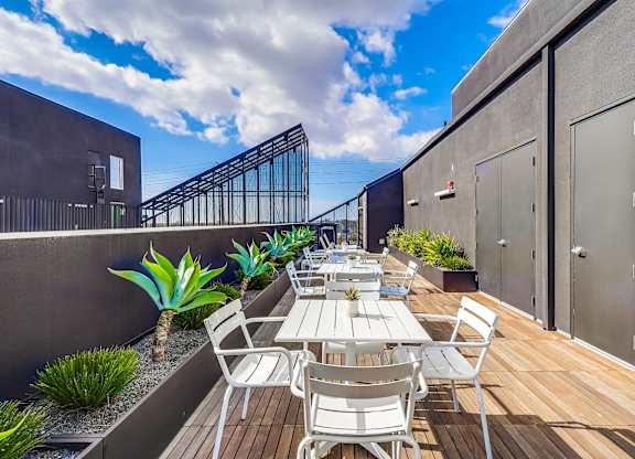 A patio with a table and chairs is surrounded by plants and a metal railing.