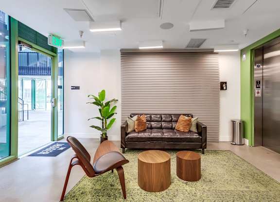 A modern living room with a grey couch, wooden chair, and a green rug.