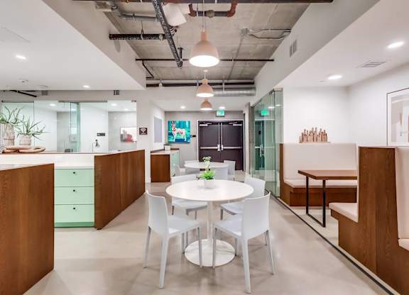 A modern office space with a glass wall and a white table surrounded by white chairs.
