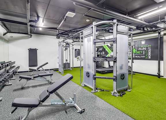 A gym with a green floor and white walls has a variety of equipment including weights and a treadmill.