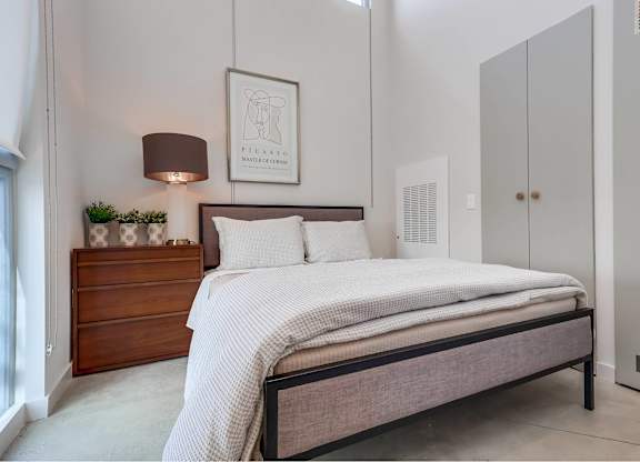 A bedroom with a bed, nightstand, and a framed picture on the wall.