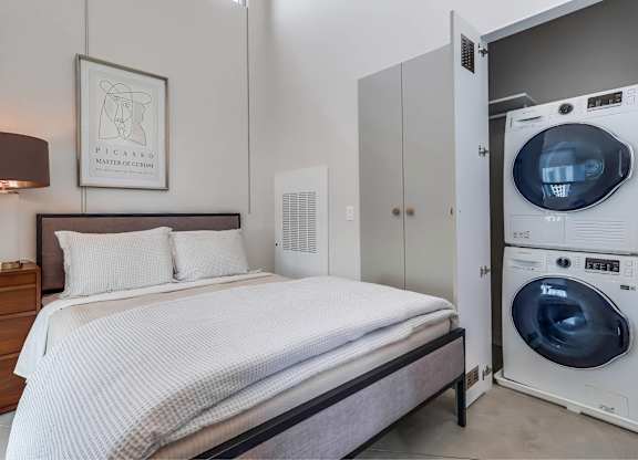 A bedroom with a bed, a washing machine, and a nightstand.