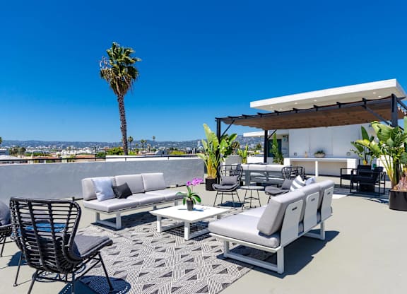 A patio with a white couch, chairs, and a table with a view of the city.