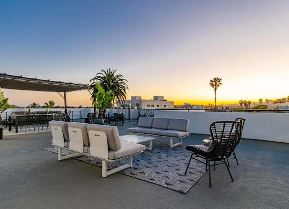 A patio with a white couch, a black chair, and a potted plant.