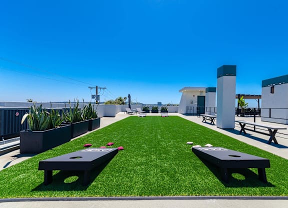 A sunny day rooftop deck with a lawn and two corn hole game wooden panels.