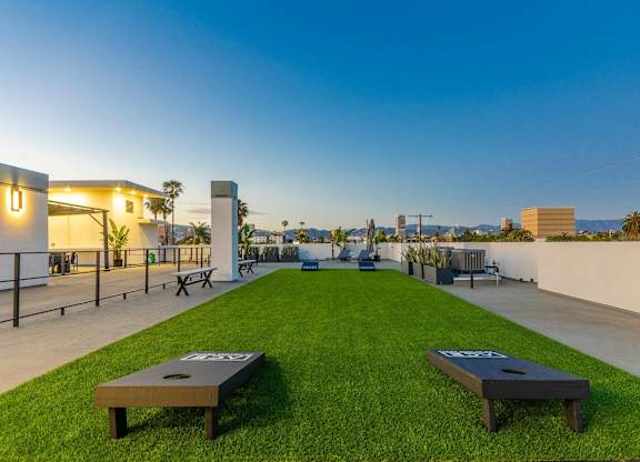 A rooftop deck with a lawn and two corn hole game wooden panels.