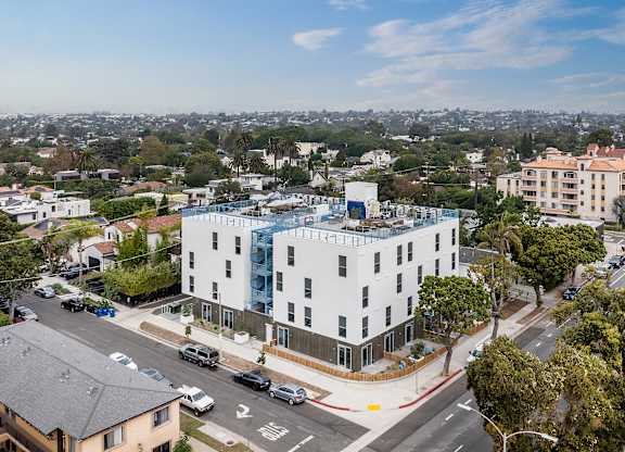 A white building with a blue glass addition sits on a street corner with cars parked on the side.