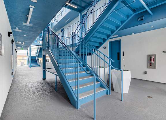 A blue staircase in a building with a white wall and a fire extinguisher.