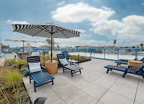 A patio with blue chairs and a striped umbrella.