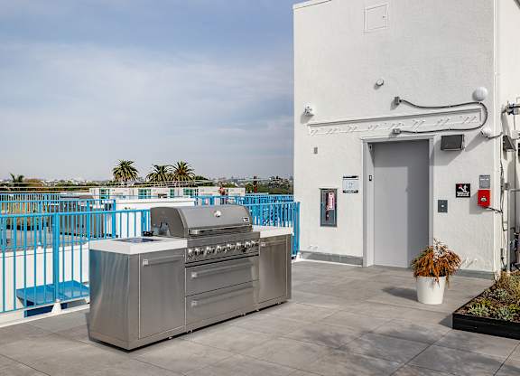 A white building with a blue fence and a grill in front of it.