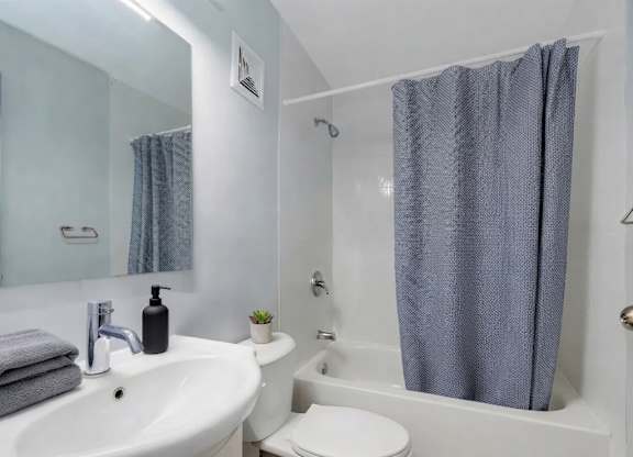 A white sink with a grey towel and a black soap dispenser on top of it.