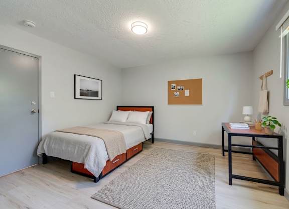 A bedroom with a bed, nightstand, and a table with a plant on it.