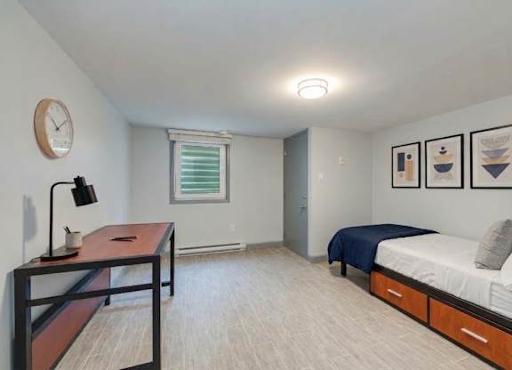 A bedroom with a bed, desk, and clock on the wall.