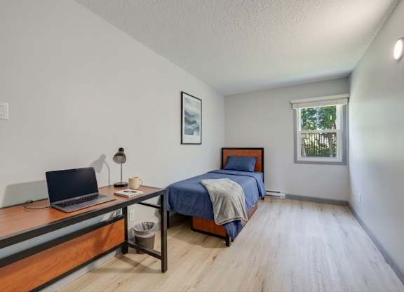 A bedroom with a bed, desk, and laptop.