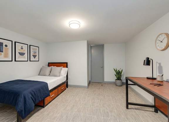 A bedroom with a bed, desk, and artwork on the wall.