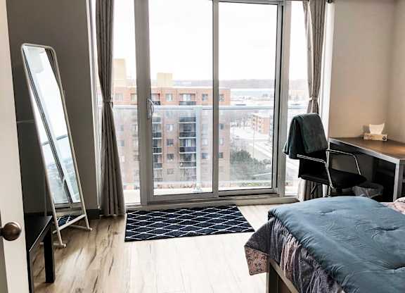 A bedroom with a large bed, desk, and a view of the city through the window.