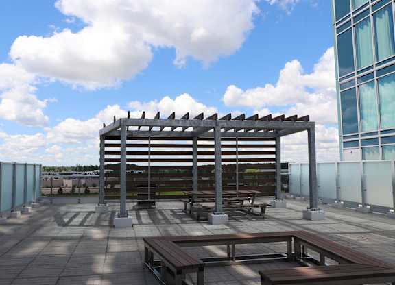 A wooden pergola with a metal frame is situated on a rooftop with benches and picnic tables.