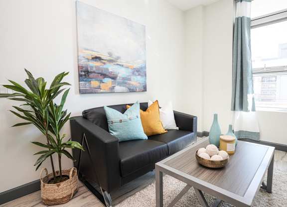 A living room with a black couch, a wooden coffee table, and a large painting on the wall.
