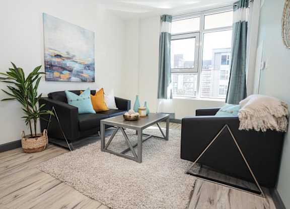 A living room with a black couch, a coffee table, and a large painting on the wall.