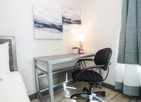 A bedroom with a bed, desk, chair, and a painting on the wall.