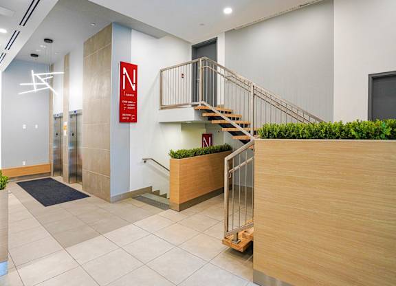 A hallway with a staircase and a red sign with a white N on it.