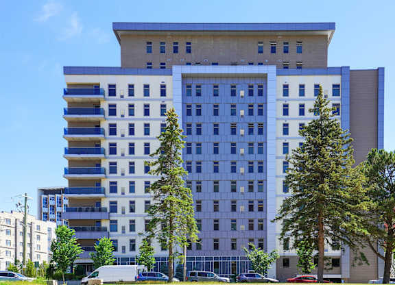 A large building with a blue and white facade is surrounded by trees and cars.