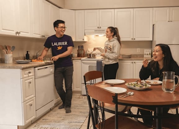 A man in a Laurier shirt is cooking in a kitchen with two women.