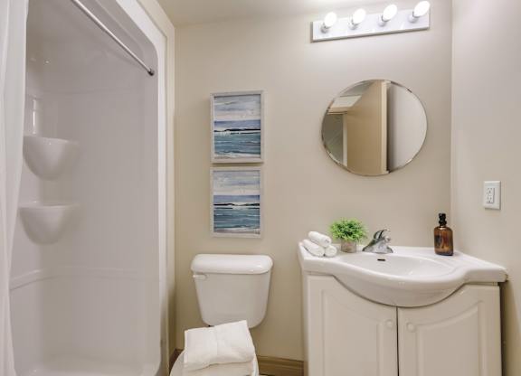 A white bathroom with a toilet, sink, mirror, and lights.